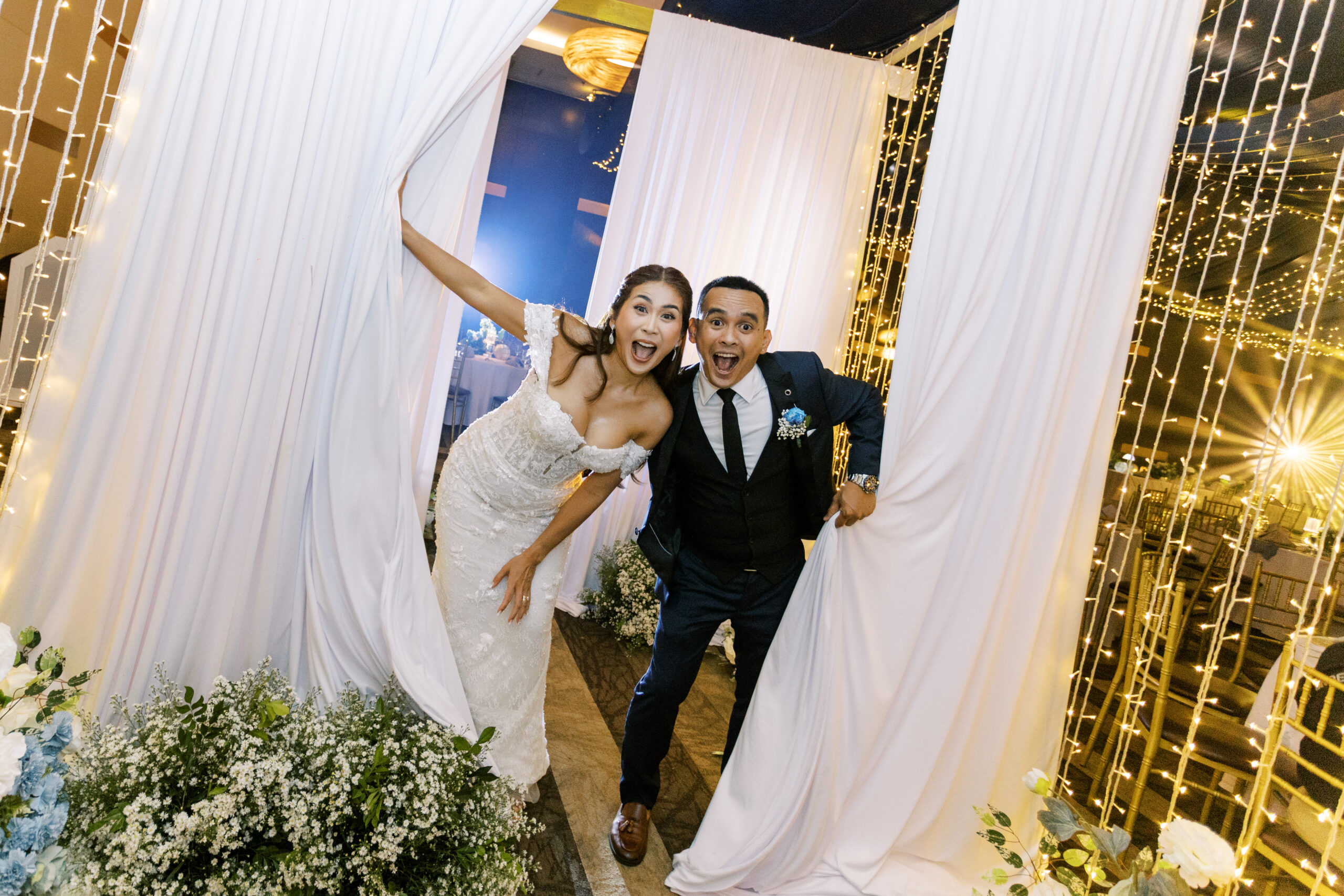 Newlyweds celebrating their grand entrance through draped curtains and fairy lights at a Bayfront Hotel Cebu wedding reception